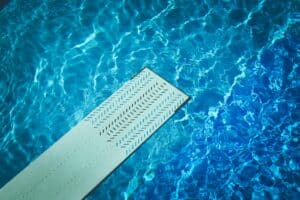 Vue plongeante sur l'eau bleue turquoise d'une piscine avec un plongeoir gris antidérapant, symbolisant la qualité de l'étanchéité et le plaisir de la baignade.